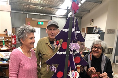 People standing around a wooden Christmas tree
