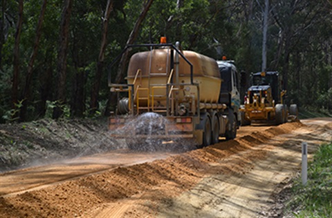Gravel resheeting in progress with grader and water sprayer truck working